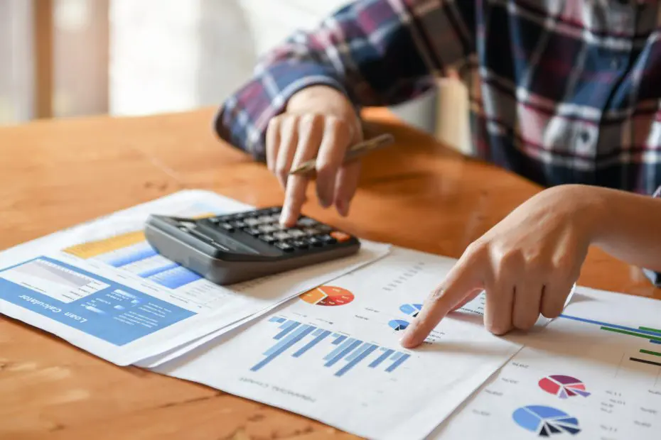 Hand pointing at graph and other hand holding pen and pressing the calculator