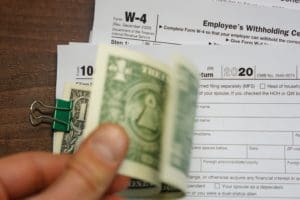 Fingers holding dollar bills clipped to 1040 tax document