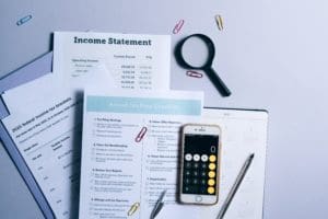 iPhone with the calculator app open on top a calendar and papers titled annual tax prep checklist, 2020 federal income tax brackets and an income statement.